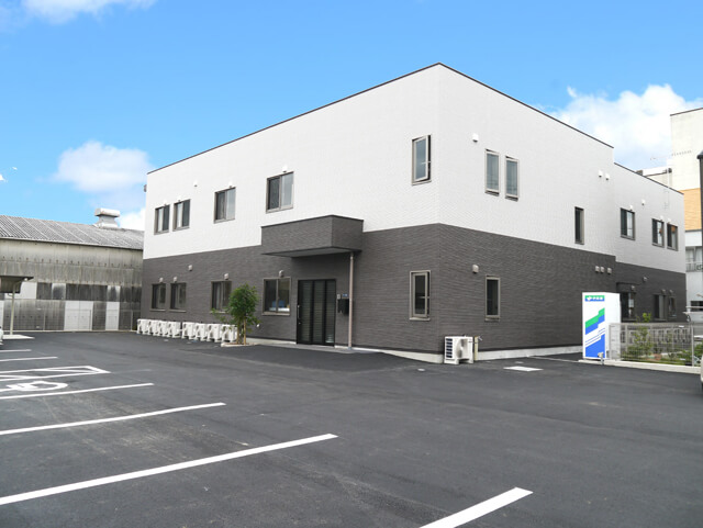 モダンデザインの介護施設建物。白と黒のツートンカラーで、駐車場完備。